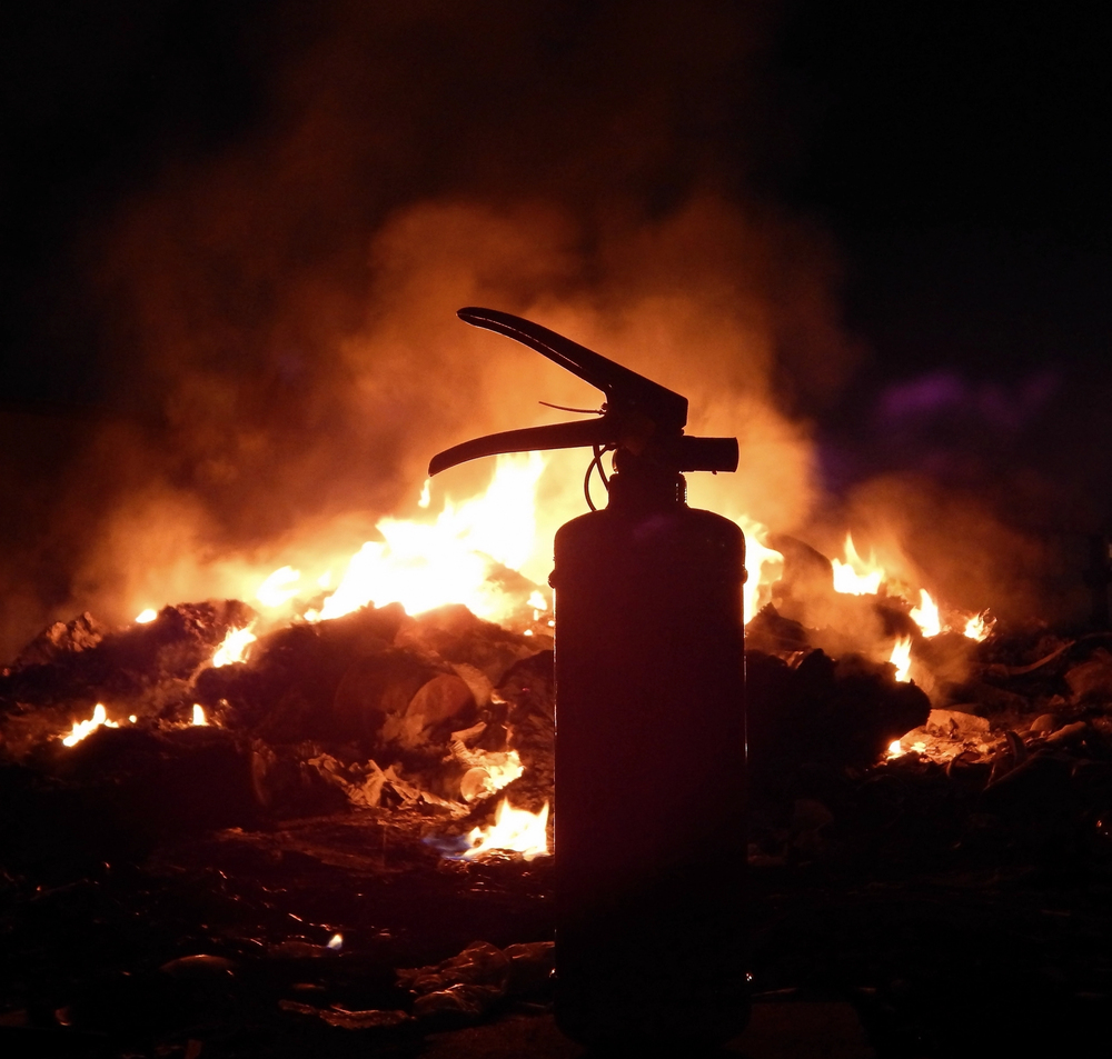 Estintore con sfondo di un cumolo di macerie in fiamme.