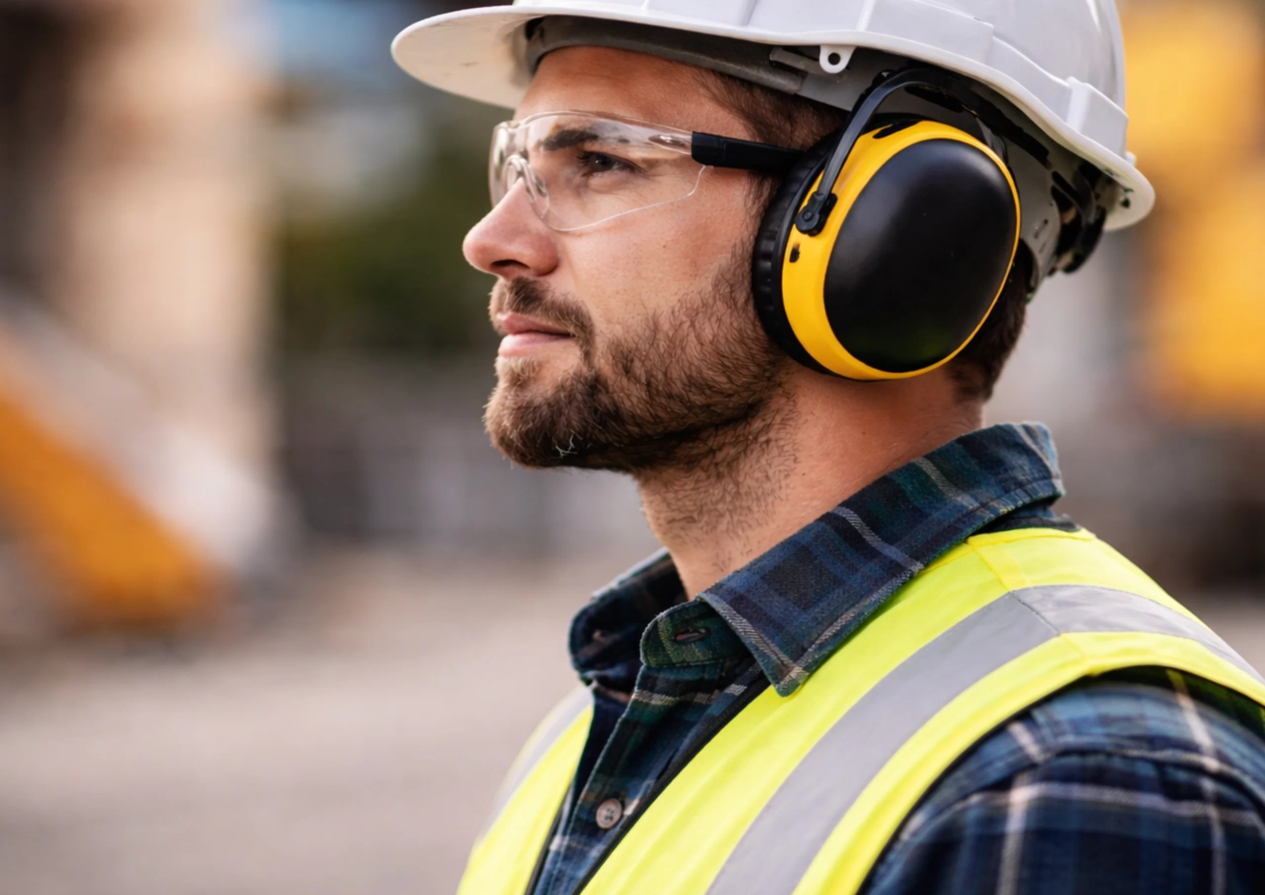Uomo di profilo con cuffie protettive in ambiente industriale